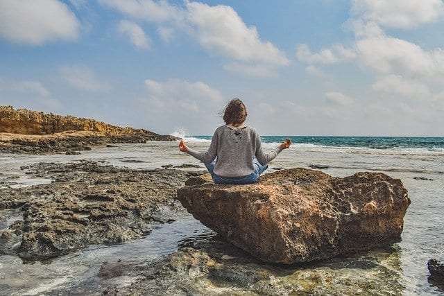 girl meditating on a rock at the beach